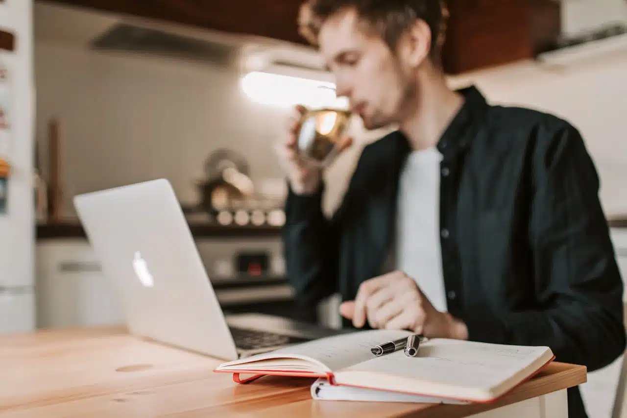 a man working on laptop at home a note book and pen is opened beside him to note down important points for his remote job