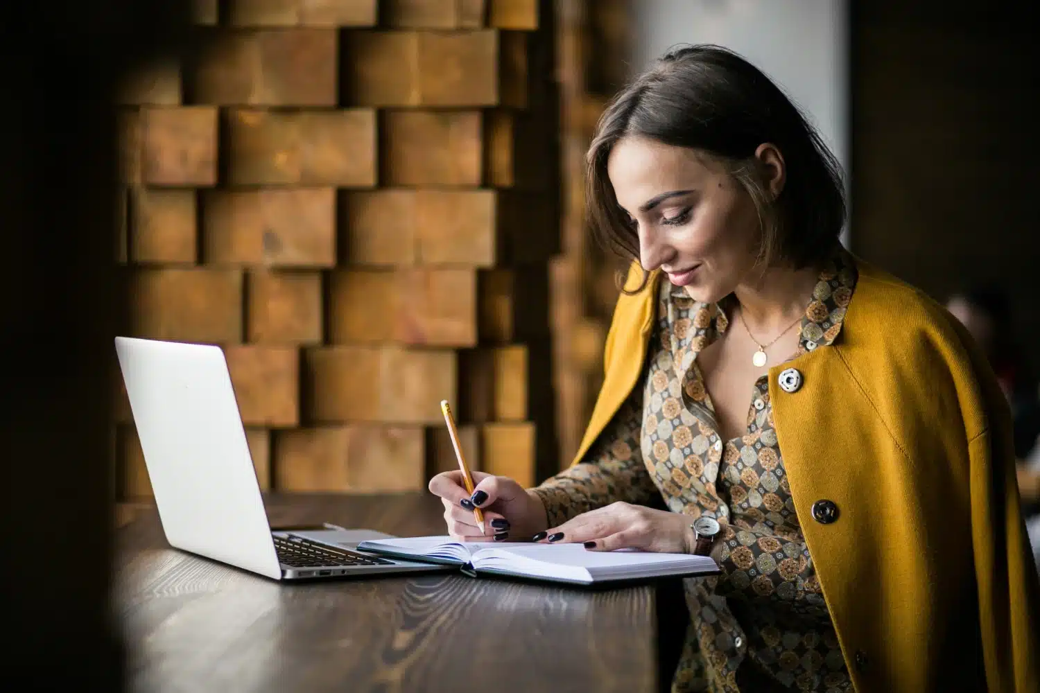 a lady working on laptop and writing on the writing pad noting down important points as she works for content writing internship